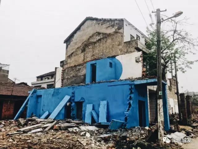 △ 這棟建筑是臨江最近的半拆遷建筑物的遺留，沅江和堤壩成為了展覽的天然背景。創(chuàng)作團(tuán)隊(duì)對(duì)這棟建筑進(jìn)行了半涂裝，將符號(hào)性的沅水曲線與拆遷進(jìn)行中的建筑立面進(jìn)行意義的疊造，它們共同觸發(fā)了場(chǎng)所空間多元語(yǔ)境的生成，把拆遷這種暫時(shí)破壞性、干擾性的介入行動(dòng)與沅水右岸發(fā)展的未來(lái)性、美好性緊密融合。